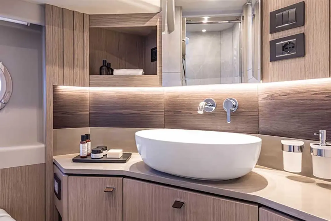 Modern bathroom featuring a stylish oval sink, wooden cabinetry, and elegant toiletries on a black tray.